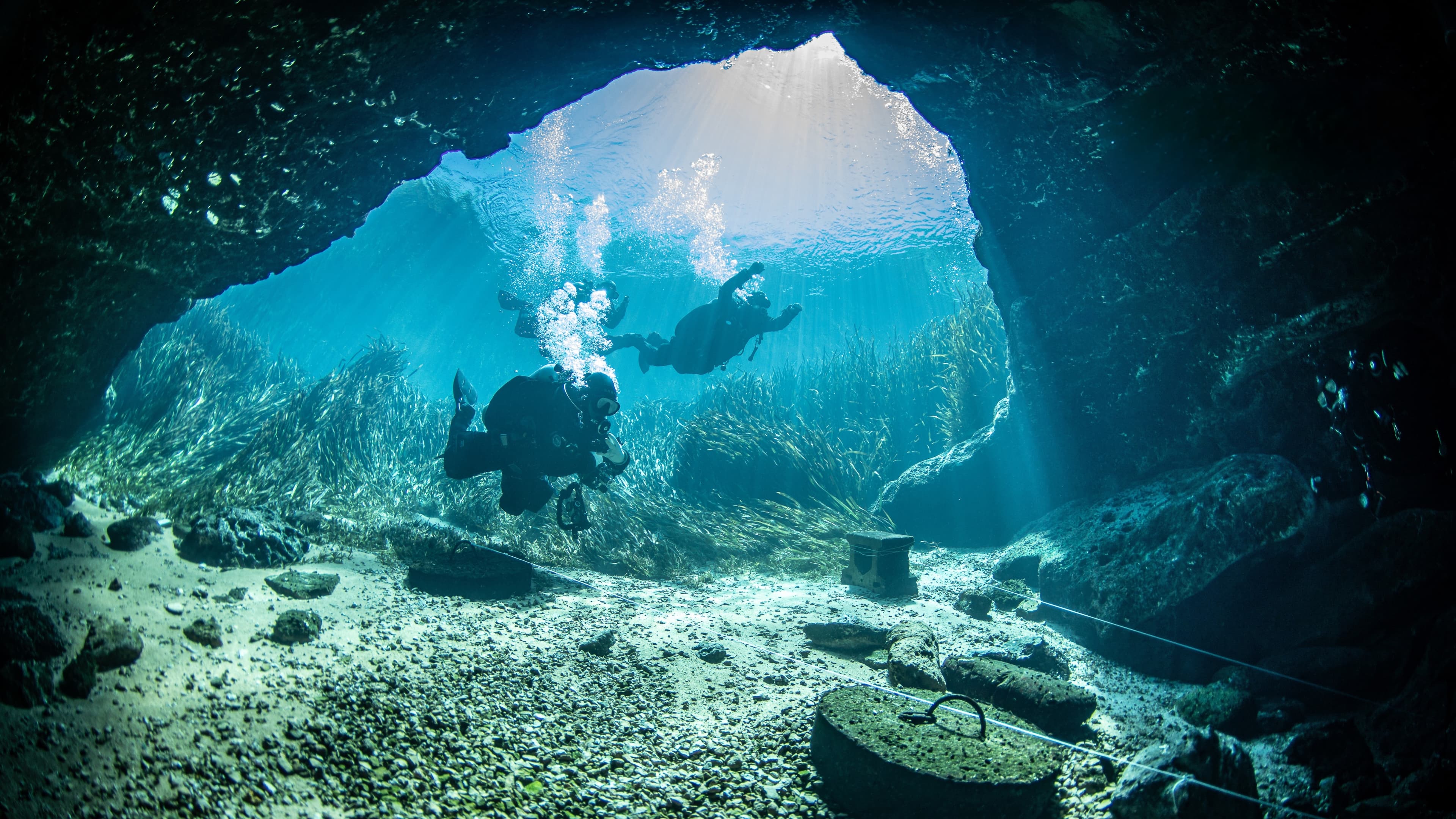 Two divers exploring a sunlit cave in control and as a team